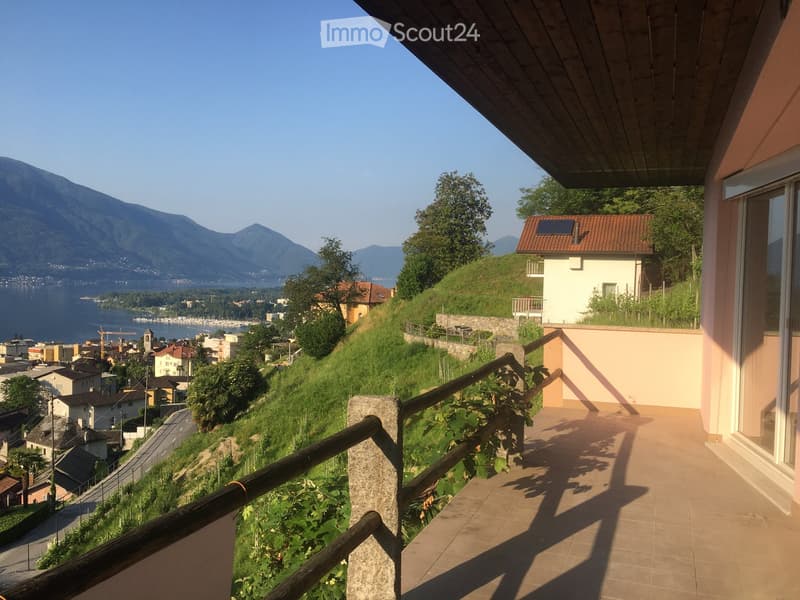 Balcony with wooden railing, overlooking a scenic lake and mountain landscape.