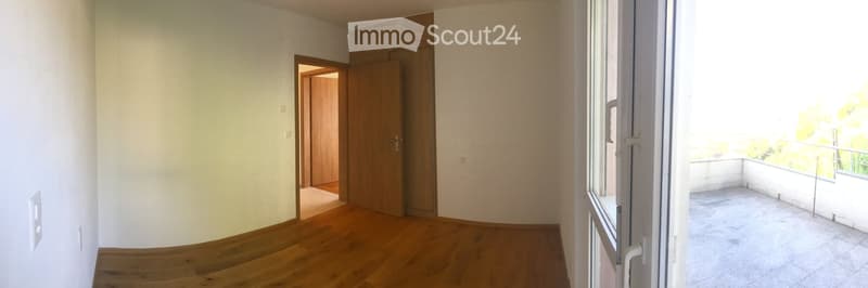 Empty room with wooden flooring, white walls, and a sliding door leading to a tiled balcony.
