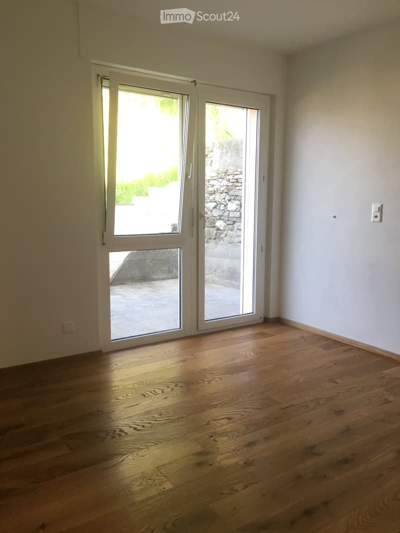 Empty room with wooden flooring and large sliding glass doors leading to an outdoor area.