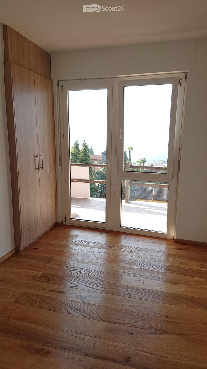 Empty room with wooden flooring, large sliding glass doors leading to a balcony or terrace, and a built-in wardrobe on one side.