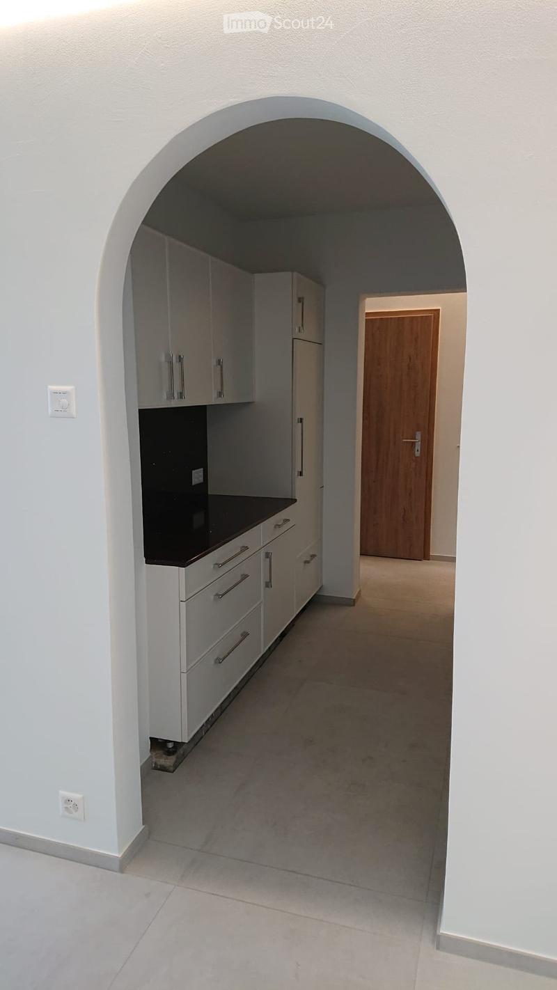 Empty kitchen area with white cabinets, a black countertop, and a wooden door leading to another room.