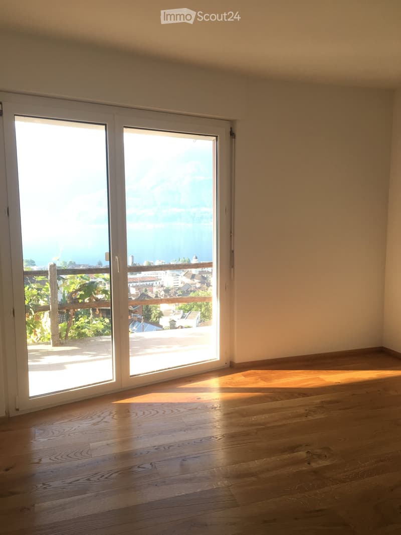 Empty room with wooden flooring and large sliding glass doors leading to a balcony with a scenic view of the city and sea.