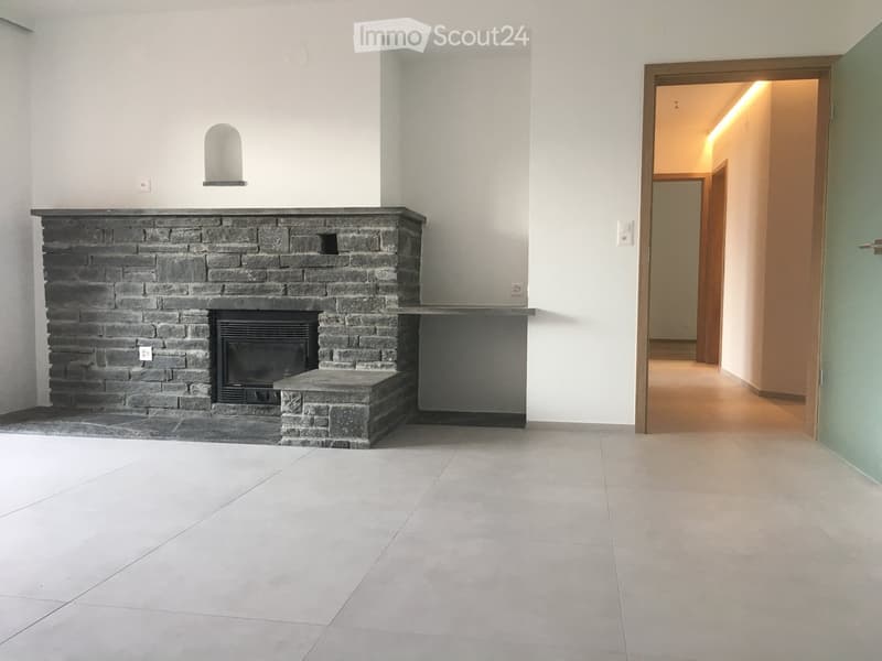 Empty hallway with tiled floor, white walls, and a stone fireplace with a built-in TV. A doorway leads to another room.