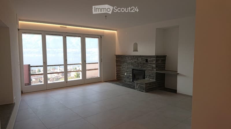 Empty room with tiled floor, stone fireplace, large sliding glass doors leading to a balcony with a scenic view.