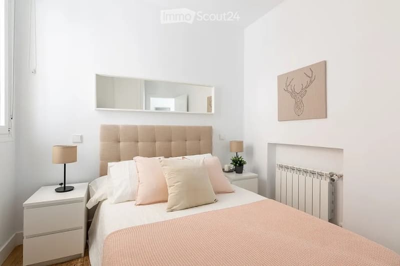 A modern, minimalistic bedroom with a large bed, pink bedding, nightstands, lamps, a mirror, and a decorative picture frame on the wall.