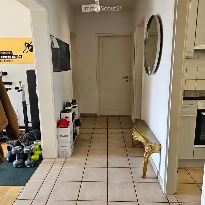 Hallway with tiled floor, white walls, a closed door, a decorative console table, and a mirror on the wall. Exercise equipment and shoes are stored on the left side.