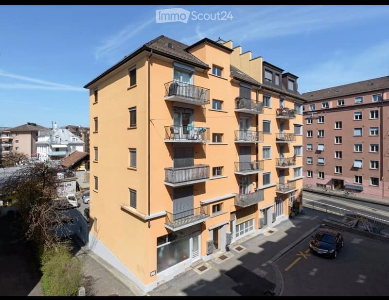 Multi-story residential building with yellow facade, multiple balconies, and surrounding urban environment.