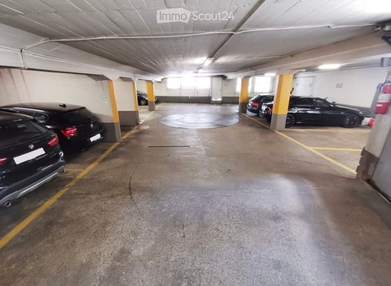 Underground parking area with several parked cars, yellow painted lines, and structural pillars.