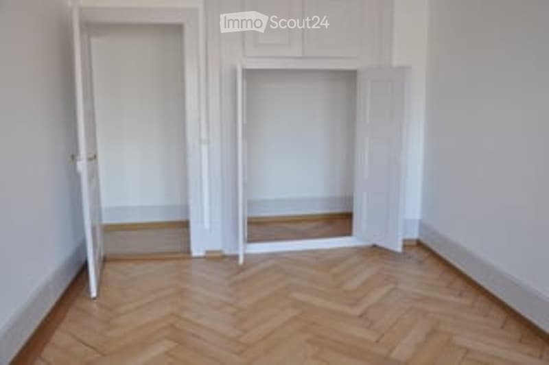 Completely empty room with white walls, wooden herringbone flooring, and an open closet with empty shelves.