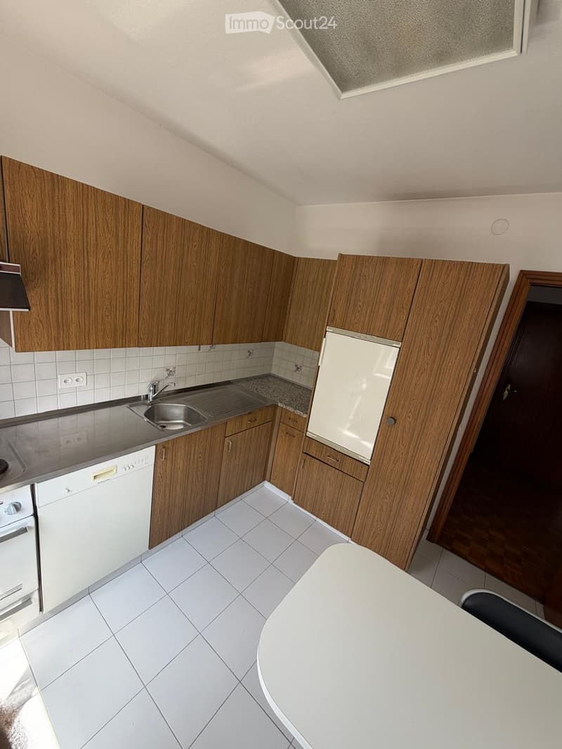 Modern kitchen with white tiled floor, wooden cabinets, stainless steel sink, dishwasher, and refrigerator.