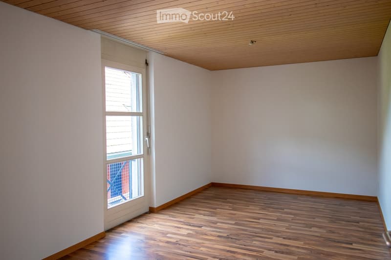 Empty room with wooden flooring, white walls, and a large window with blinds. The ceiling is finished with wood paneling.