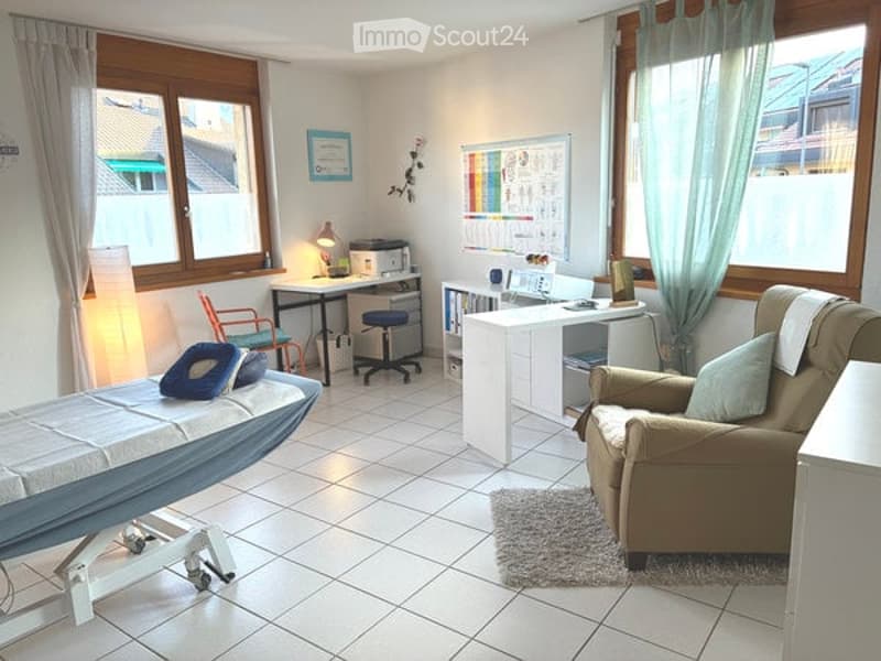 Well-lit room with large windows, a sofa, a small table, a cabinet, a lamp, and a screen. The space appears to be a living or study area with a cozy and organized setup.