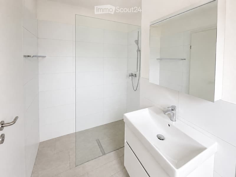 Modern bathroom with white tiles, a glass-enclosed shower, a white sink with a modern faucet, and a large mirror above the sink.