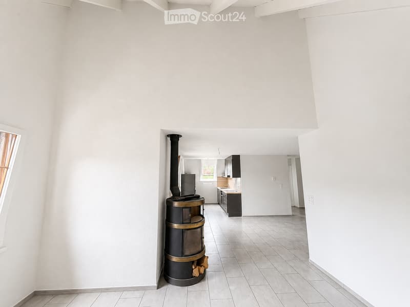 Open-plan living and kitchen area with a wood stove, tiled floor, and modern kitchen cabinets.