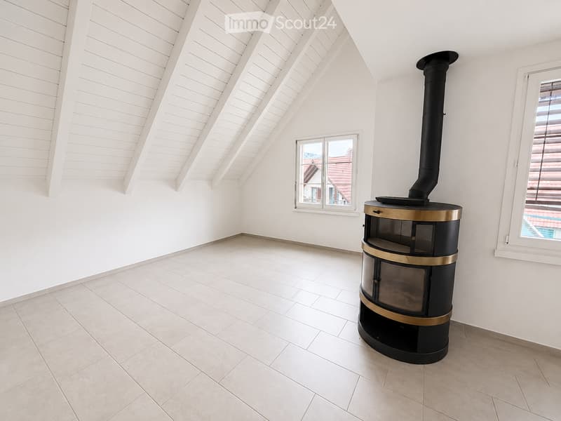 Empty room with white walls, light-colored tiled floor, and a modern wood-burning stove with a chimney. Two windows offer views of the outside.