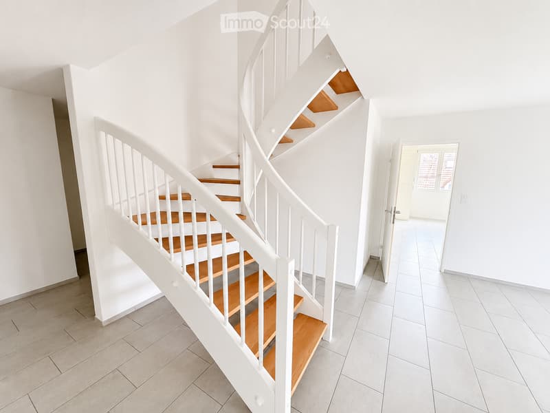 Spiral staircase with wooden steps and white railings, leading to an open doorway with white tiled flooring and walls.