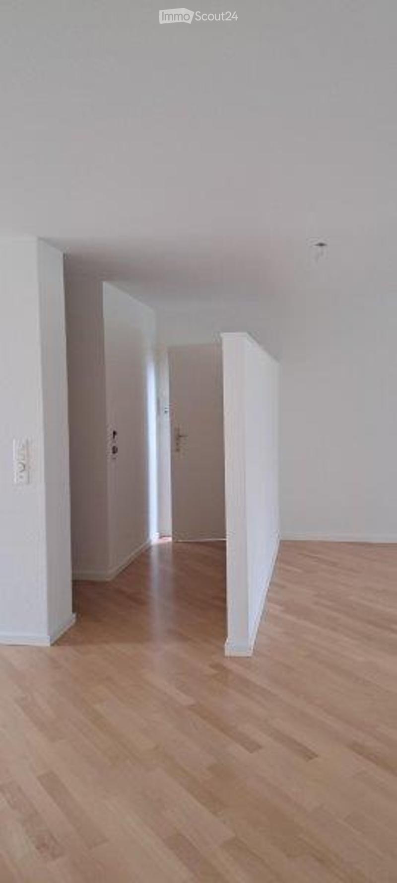 Empty room with light wooden flooring and white walls, featuring a single door at the far end.