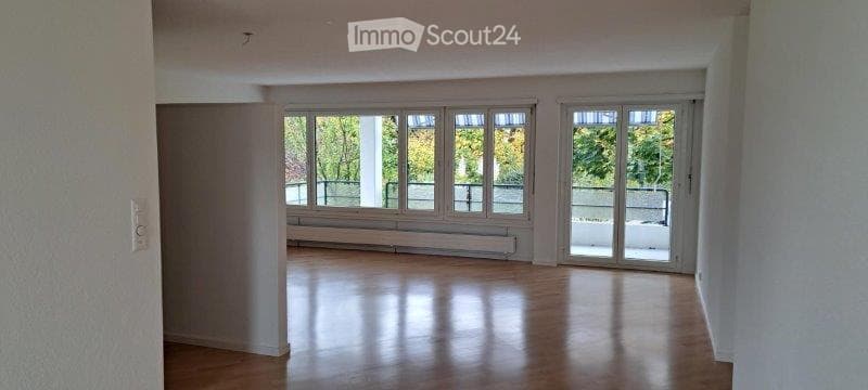 Empty room with wooden flooring, large windows, and a sliding glass door leading to a balcony.