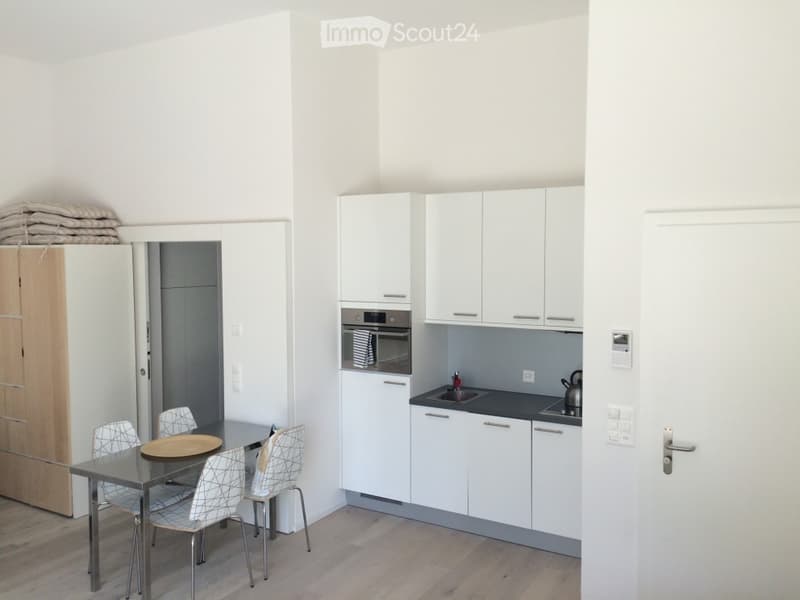 A modern, compact kitchen and dining area with white cabinets, a built-in oven, a sink, and a small dining table with chairs.