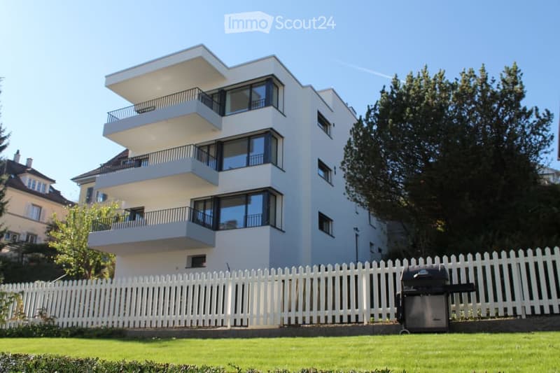 Modern multi-story apartment building with white exterior, large windows, and multiple balconies.