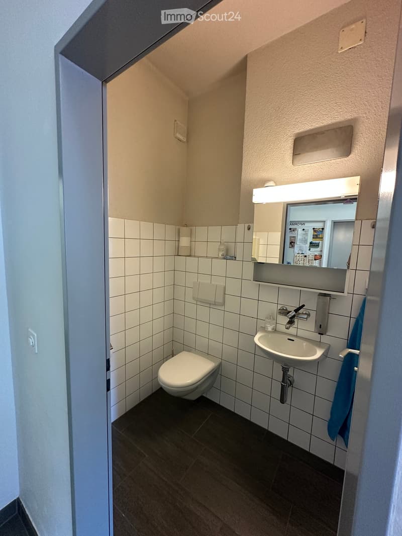 Compact bathroom with white tiled walls, a toilet, a sink with a mirror, and a towel hanging on the side.