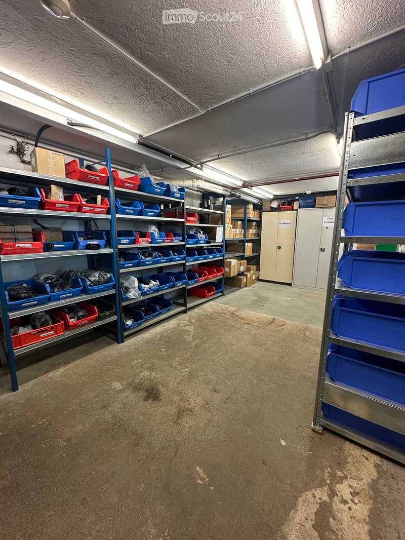 Empty storage room with metal shelving units and various storage bins, concrete floor, and industrial lighting.