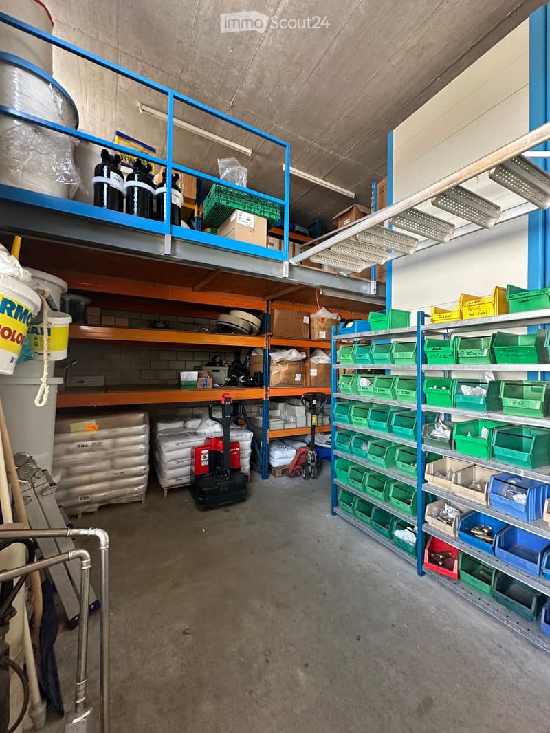 A spacious storage area with multiple shelving units filled with various items including pallets, boxes, barrels, and storage bins. A forklift is parked in the center, and the floor is concrete.