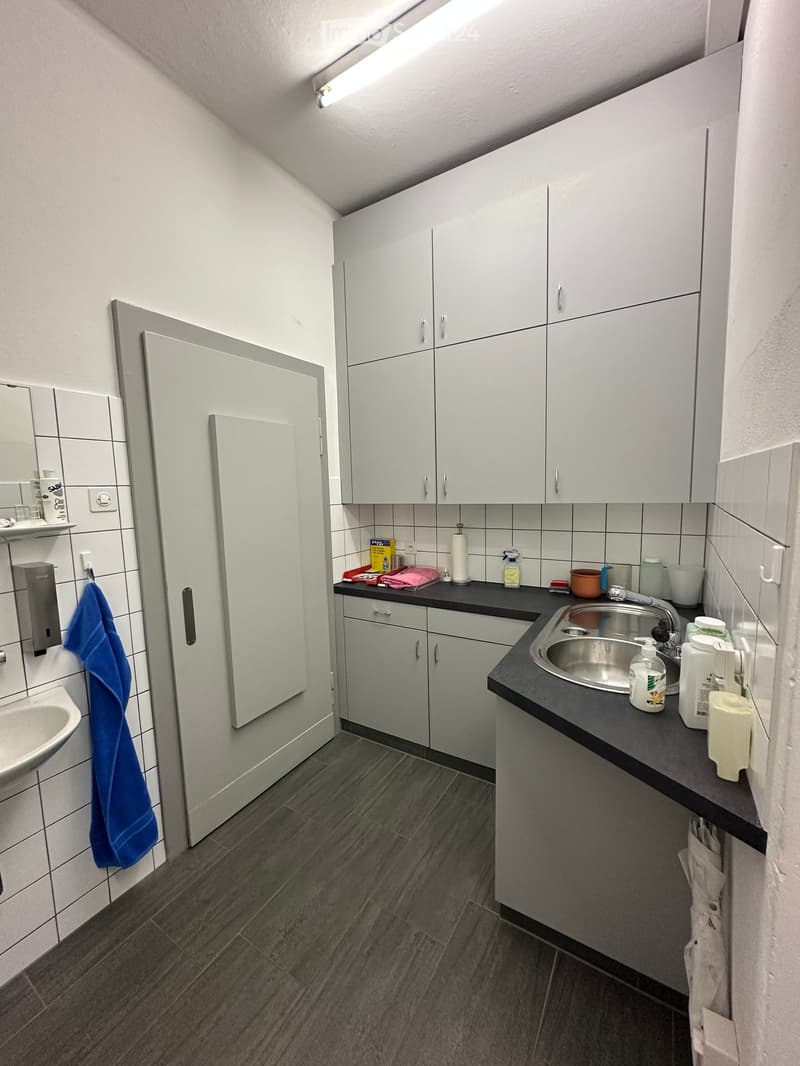 Modern bathroom with white cabinets, dark countertop, sink, and mirror. Includes a towel, cup, and bottle on the counter.