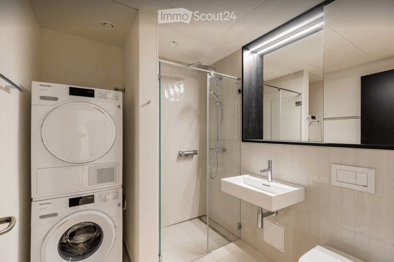 Modern bathroom with a washing machine, shower, sink, and mirror.