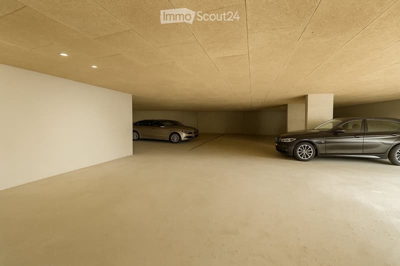 Modern underground garage with two parked cars, beige walls, and a smooth concrete floor.