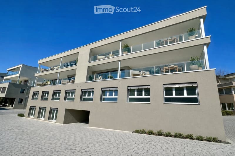 Modern multi-story building with large windows and balconies, featuring contemporary design and clean lines.