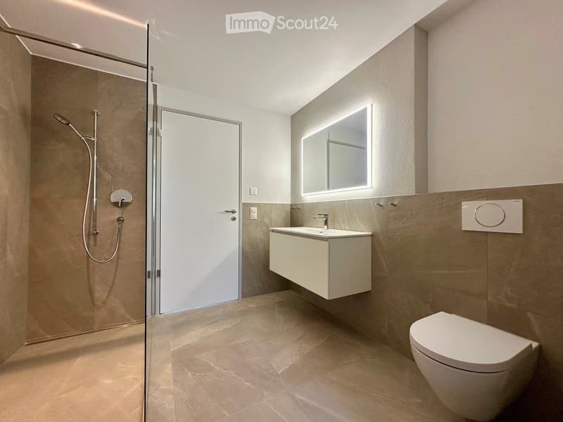 Modern bathroom with shower, sink, and toilet. Tiled floor and walls, glass door for shower, white vanity with sink, and mirror.