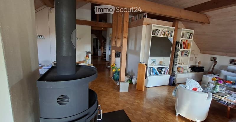 Living room with exposed wooden beams, fireplace, bookshelf, sofa, coffee table, and guitar in the corner.