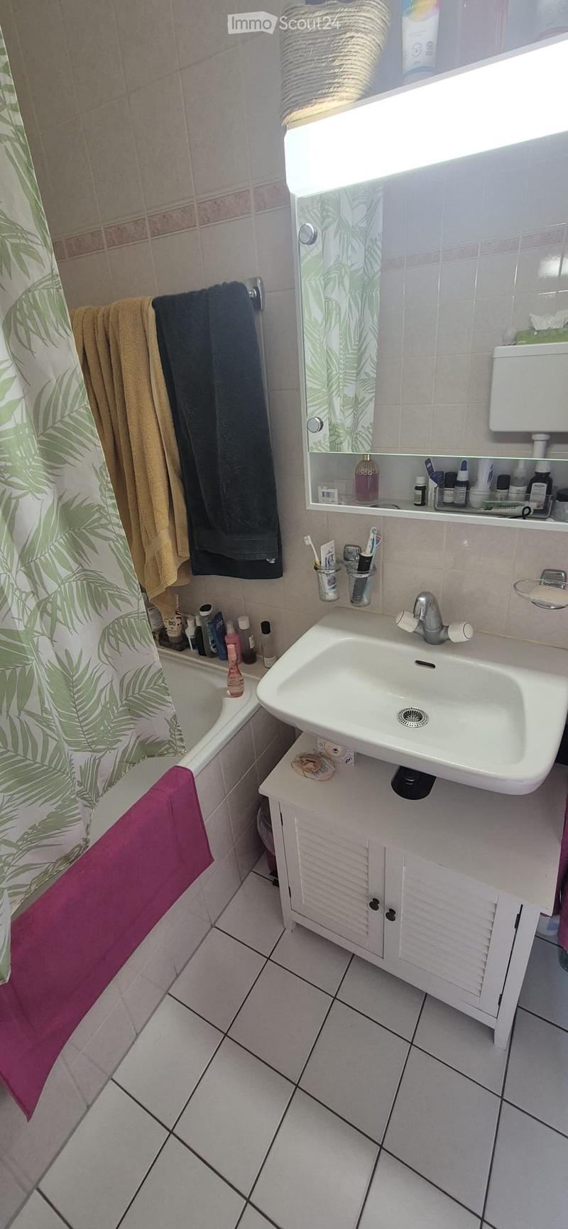 Bathroom with a white sink, mirror, cabinet, bathtub, and various toiletries. The floor is tiled, and towels are hanging on the side.