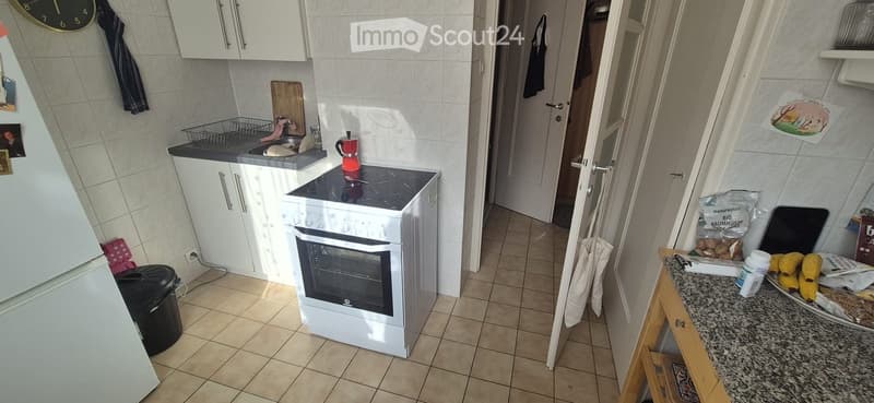 The kitchen features white cabinets, a white oven, a refrigerator, a sink, a coffee maker, and a cutting board on the counter. There is also a stool and a clock on the wall.