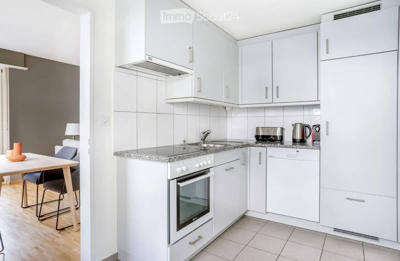 Modern kitchen with white cabinets, stainless steel appliances, and a small dining area with a table and chairs.