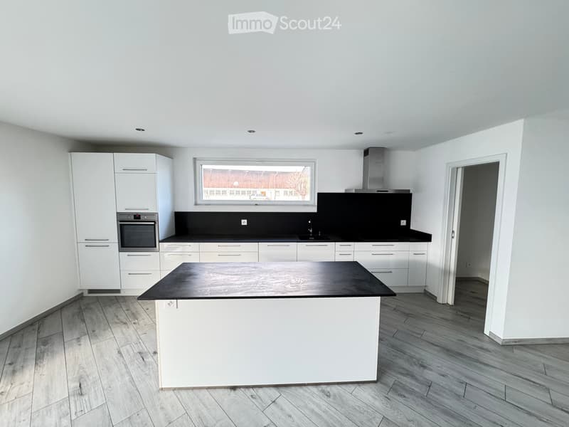 Modern kitchen with white cabinets, black countertops, a central island, and a large window offering a view.