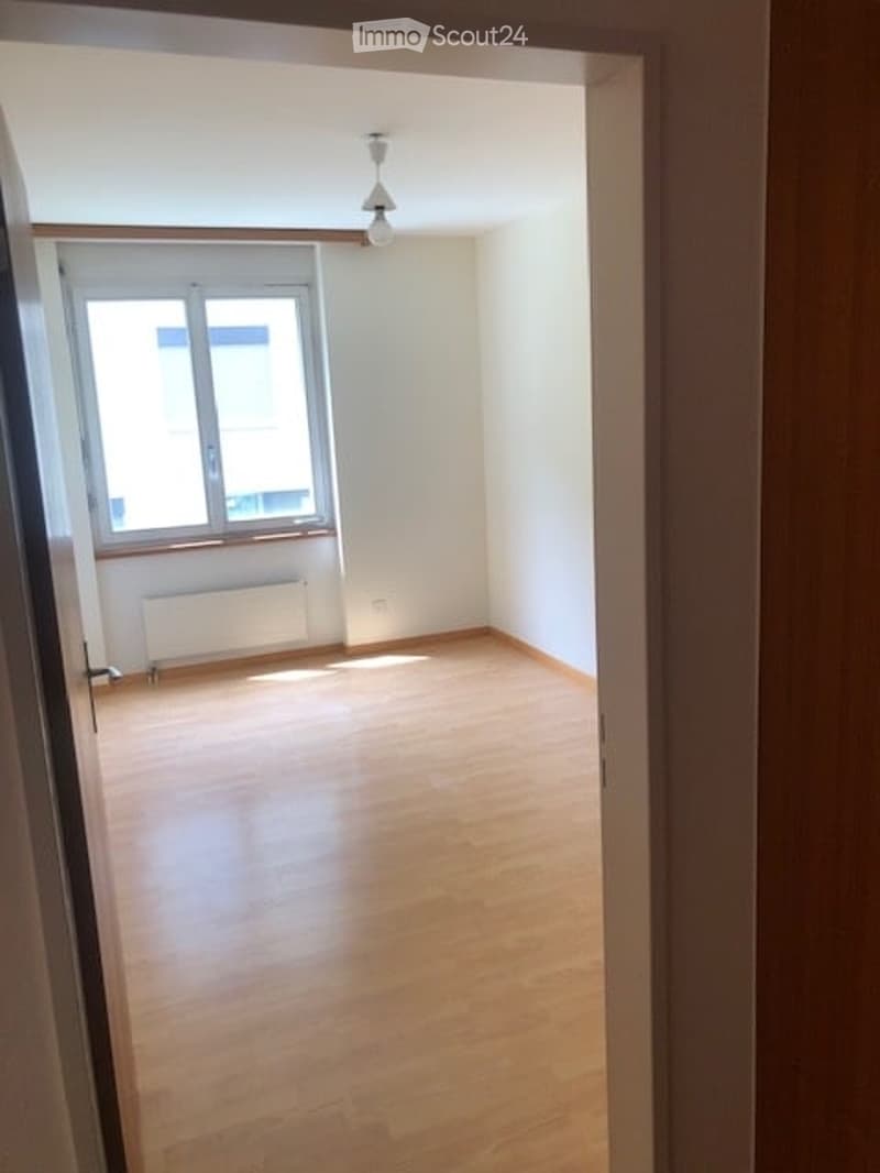 Empty room with wooden flooring, white walls, and a single window with a radiator below it. The room is unfurnished and has a simple, clean design.