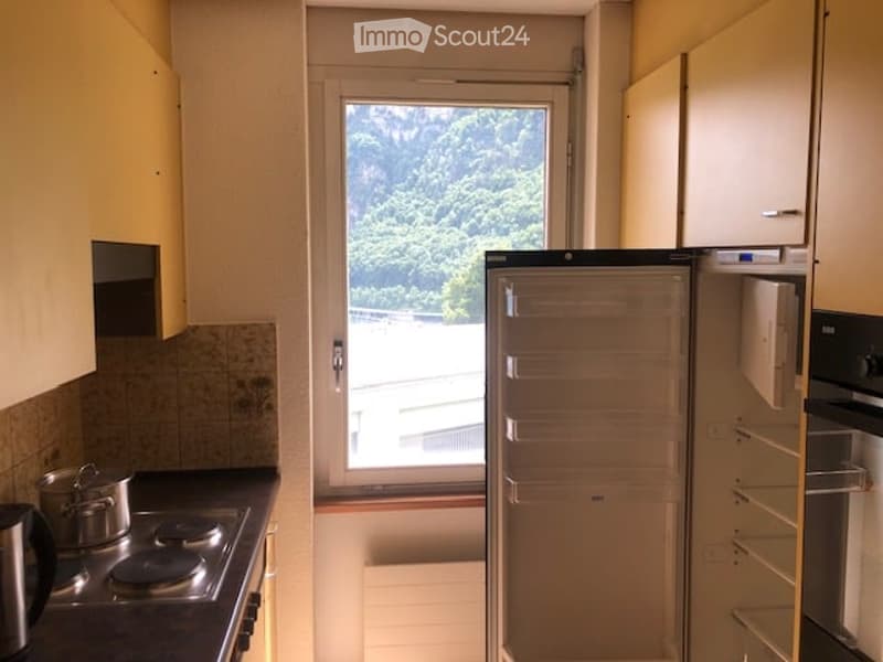 Modern kitchen with light-colored cabinets, a window offering a view of greenery, a refrigerator, stove, and a pot on the counter.