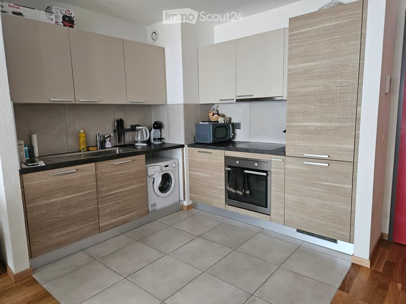 Modern kitchen with light wood cabinets, stainless steel appliances, and tiled flooring.