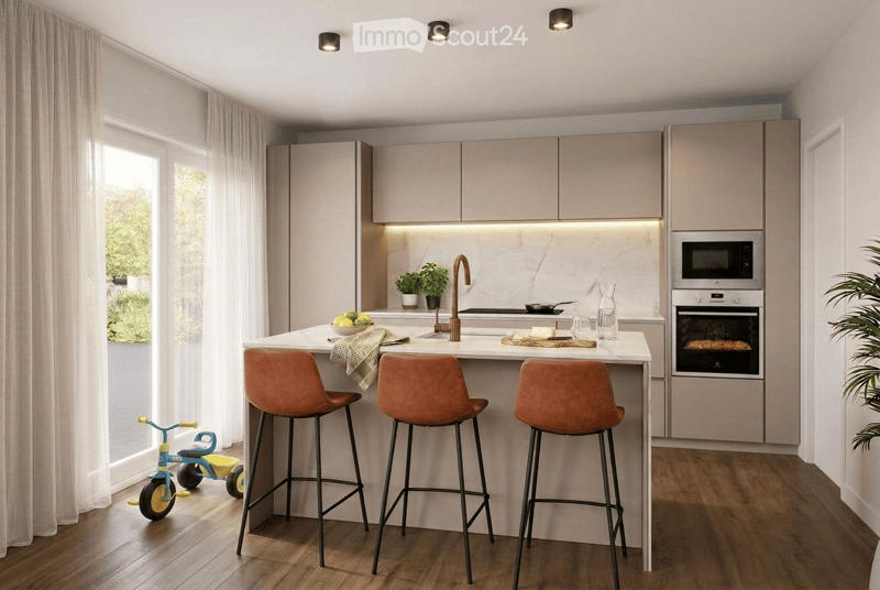 Modern kitchen with light-colored cabinets, a central island with bar stools, and built-in appliances including an oven and microwave. The island features a marble countertop, a sink with a modern faucet, and a small plant on the counter. A child's tricyc