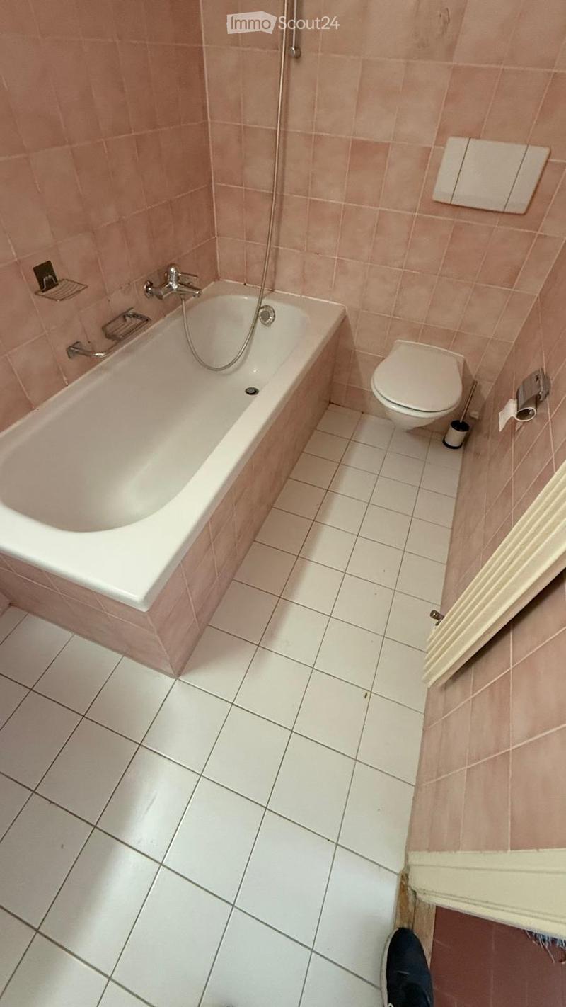 Bathroom with a bathtub, toilet, tiled walls, and a shower hose attached to the wall.
