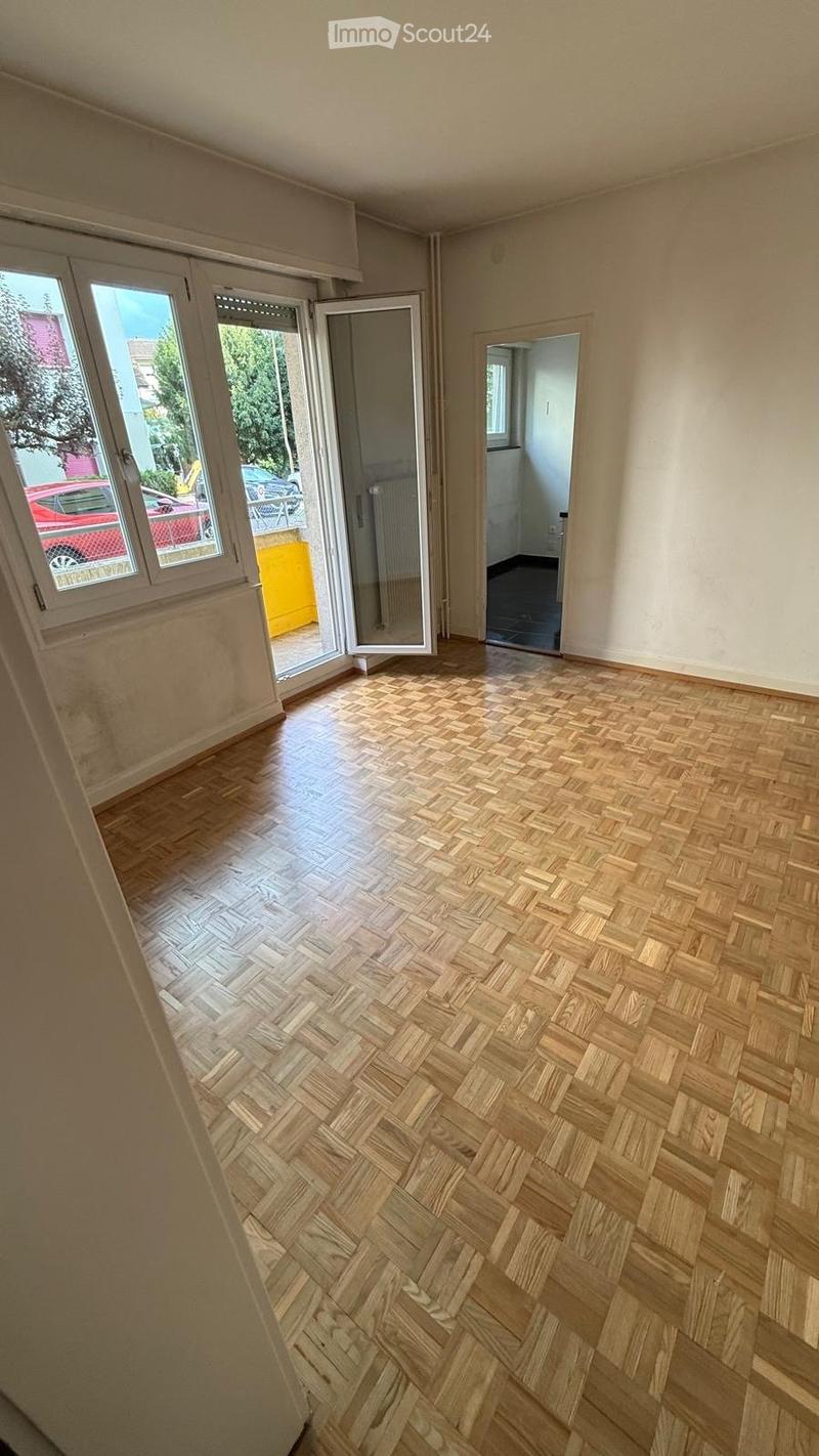 Empty room with wooden herringbone flooring, large windows, and an open doorway leading to a balcony area.
