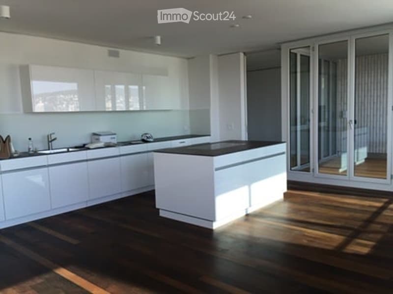 Modern kitchen with white cabinets, dark wooden floor, island, and large windows offering a view.
