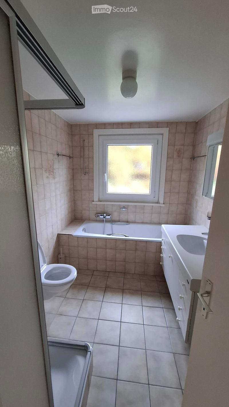 Bathroom with tiled walls and floor, featuring a toilet, bathtub, sink, and shower stall. A window provides natural light.