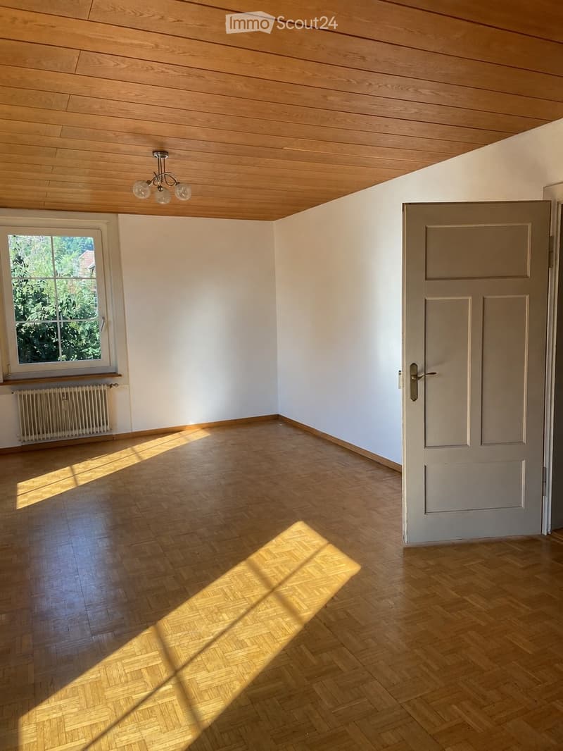 Empty room with wooden flooring, white walls, a wooden ceiling, a window with a radiator below, and a closed door.