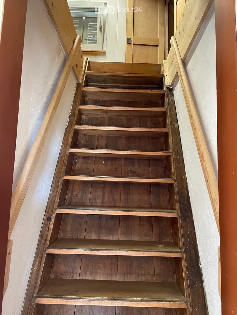 Wooden staircase with handrails and open risers, leading upwards with a visible doorway at the top.