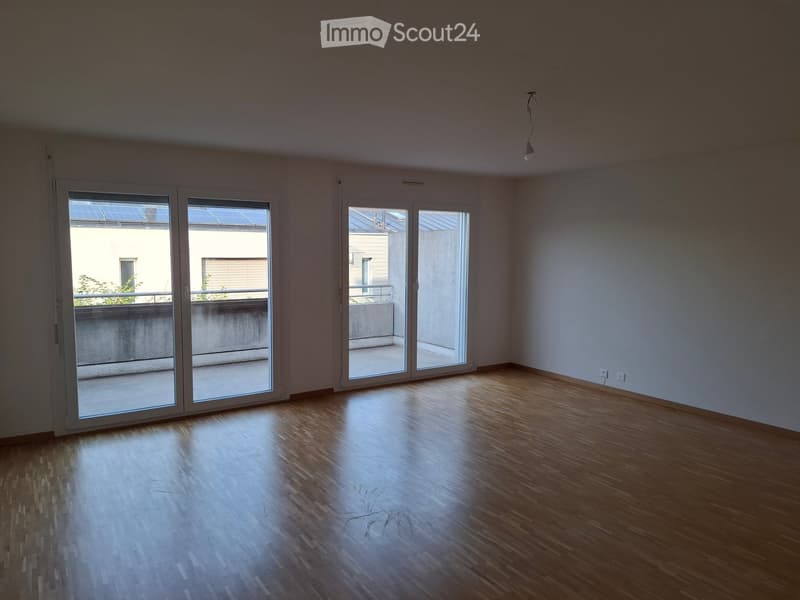 Empty room with wooden flooring, large sliding glass doors leading to a balcony, and white walls.