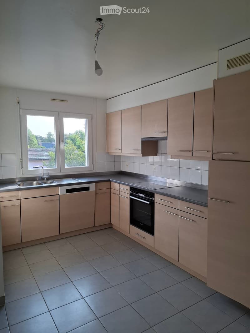 Modern kitchen with light wood cabinets, stainless steel appliances, tiled floor, and large windows.