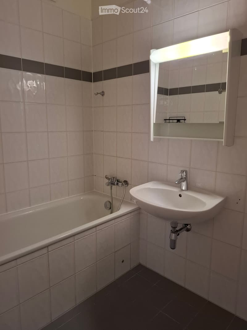 Bathroom with a bathtub, sink, mirror, and light fixture. The walls are tiled with a black and white border design.